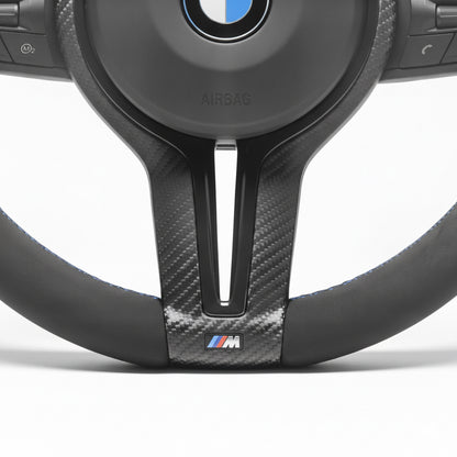 Närbild på alcantara läderklädsel med matt kolfiber, m-sport logga samt M-färgade sömmar. Bimmers™ BMW M-Sport matt kolfiber svart ratt med magnetiska paddlar F-serien.
