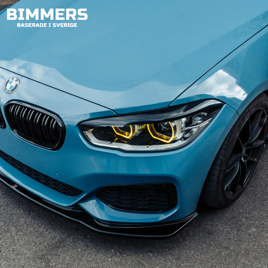 Närbild av en blå BMW F20 med gula DRL installerade