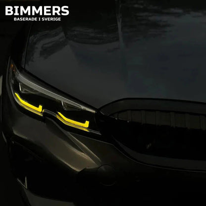 Närbild på en BMW G20 Standard LED-strålkastare med tända gula DRL-ljus i mörkret